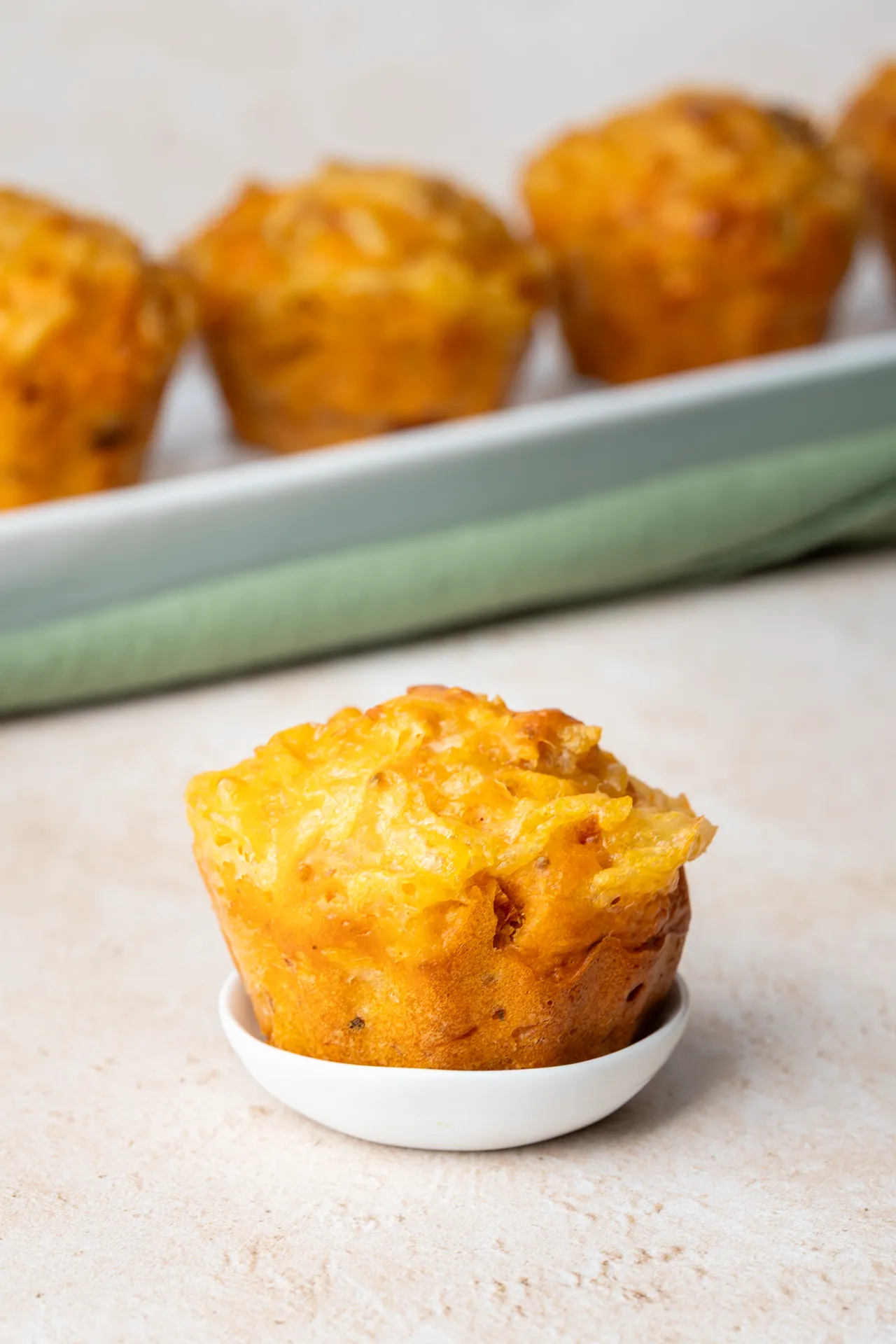 Vegane Pizza-Muffins – einfaches Rezept für Buffet, Picknick und Party 1 Pizzamuffin auf einem sehr kleinen Teller und mehrere Pizzamuffins im Hintergrund