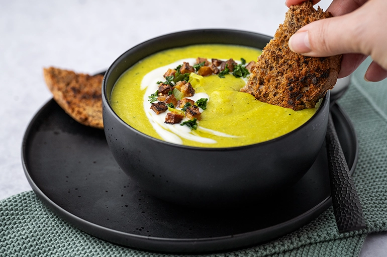 Brot eingetunkt in veganer Käse-Lauch-Suppe