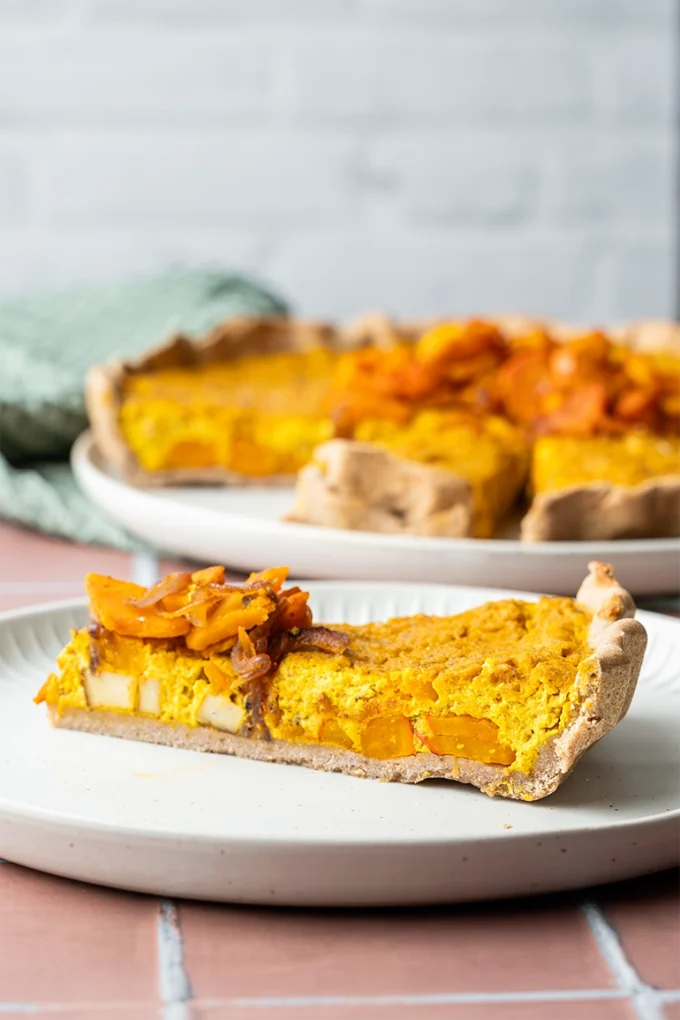 Ein Stück vegane Kürbis-Quiche auf einem hellen Teller