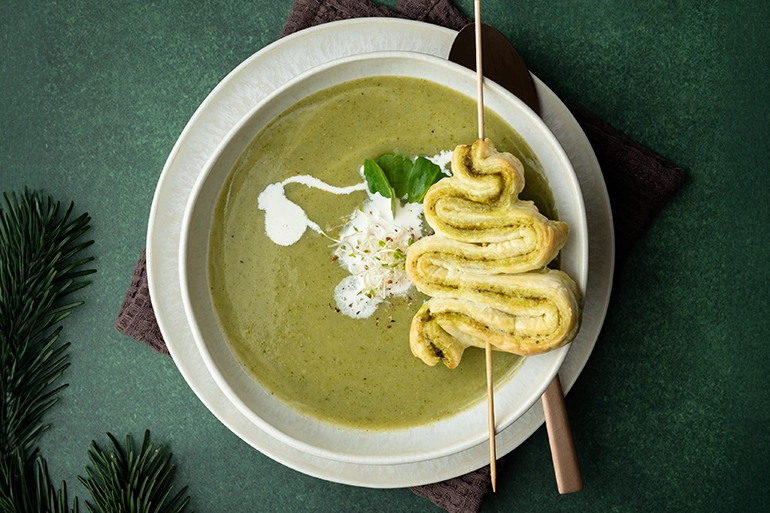 Grüne Suppe mit Sahne in einer Schale darauf ein Spieß mit einem Tannenbaum