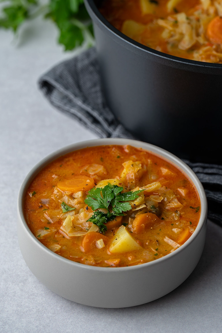 vegan_rezept_Spitzkohl_Curry_4 Eine Schale mit veganem Spitzkohl Curry neben einem Topf