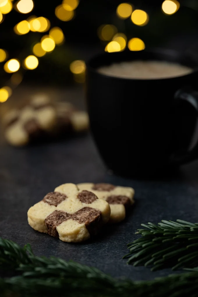 Schachbrettkekse neben einer Tasse Kaffee auf dunklem Untergrund