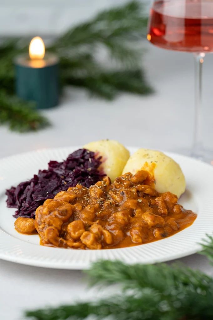 veganer Gulasch mit Rotkohl und Klößen auf einem weißen Teller