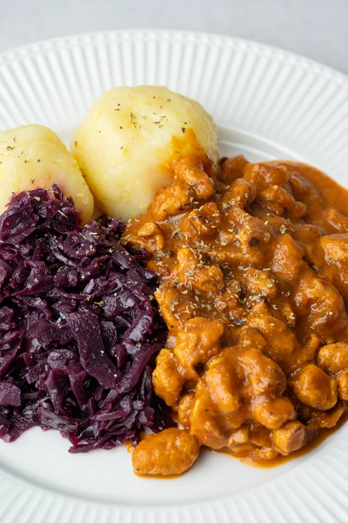 Veganer Gulasch mit Klößen und Rotkohl auf einem weißen Teller