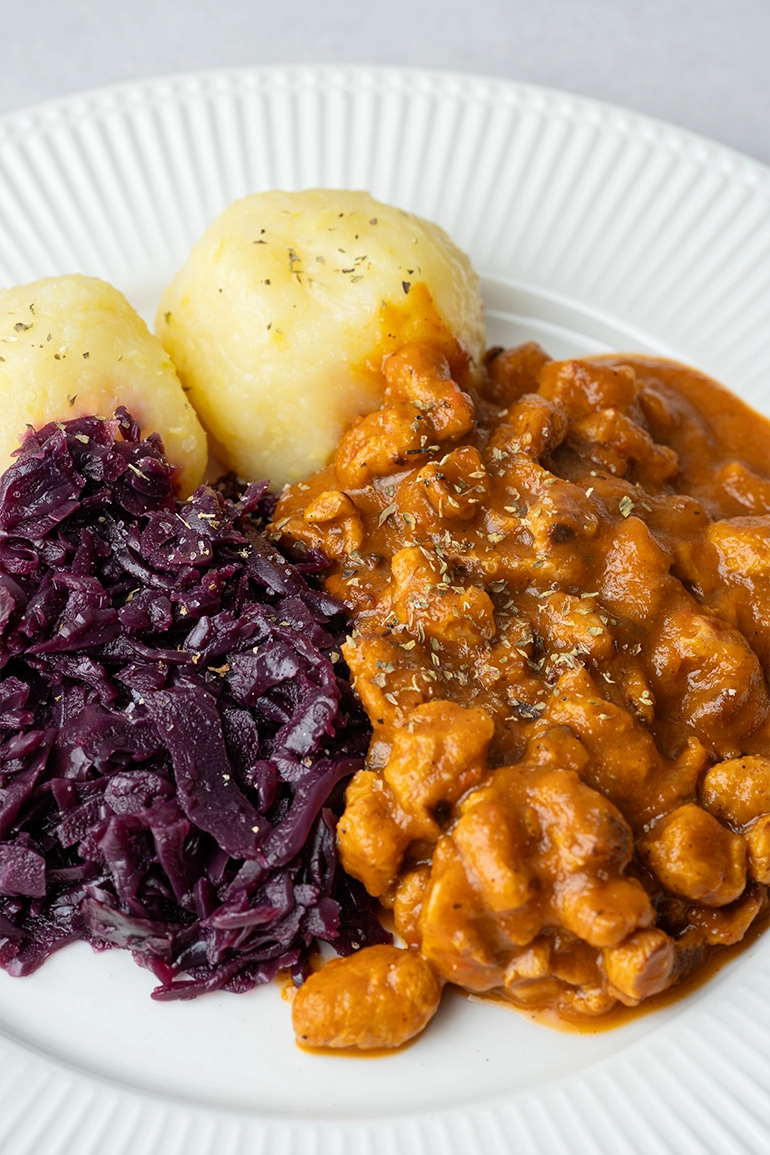 vegan_rezept_veganes_Gulasch_2 Veganer Gulasch mit Klößen und Rotkohl auf einem weißen Teller