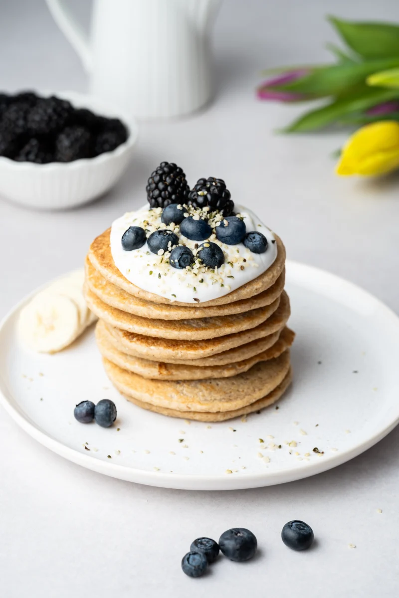 rezept-vegan-brunch-vegane-gesunde-pancakes-1 Stapel vegane gesunde Pancakes mit Blaubeeren und Joghurt auf einem hellen Teller