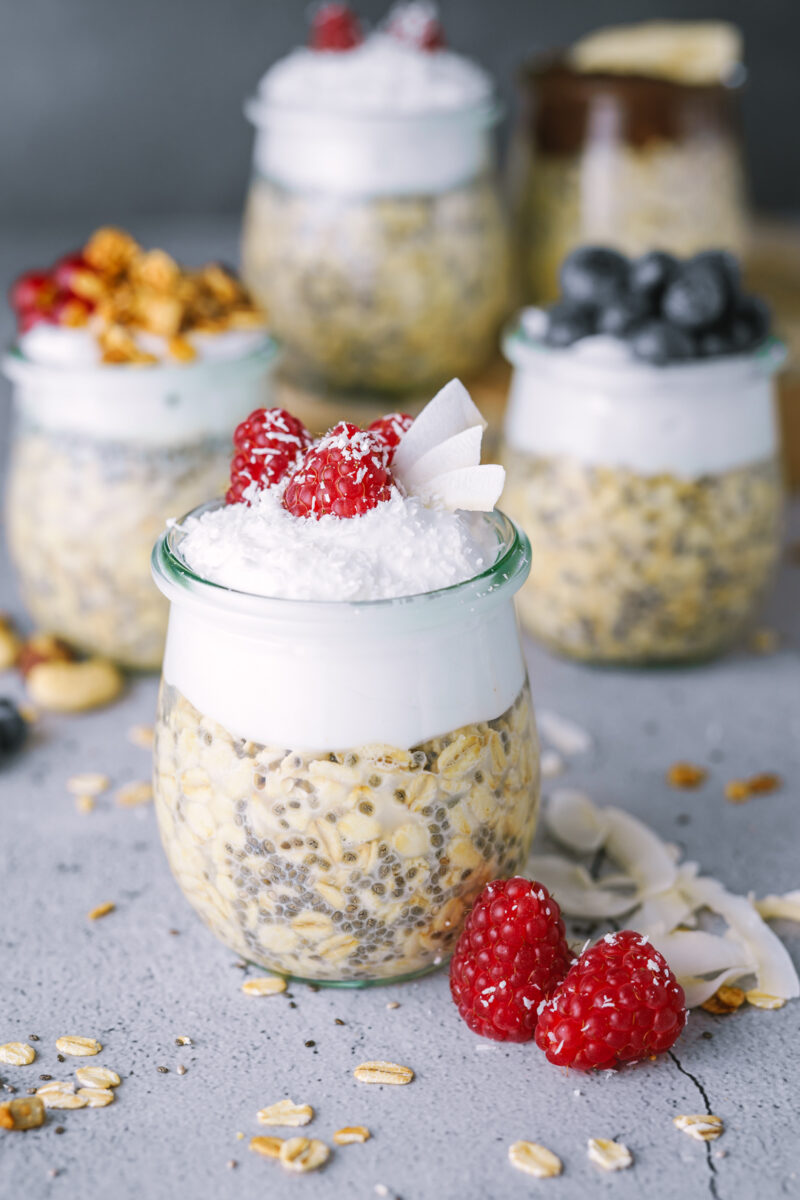 mehrere overnight oat mit Toppings wie Himbeeren, Balubeeren und Kokos
