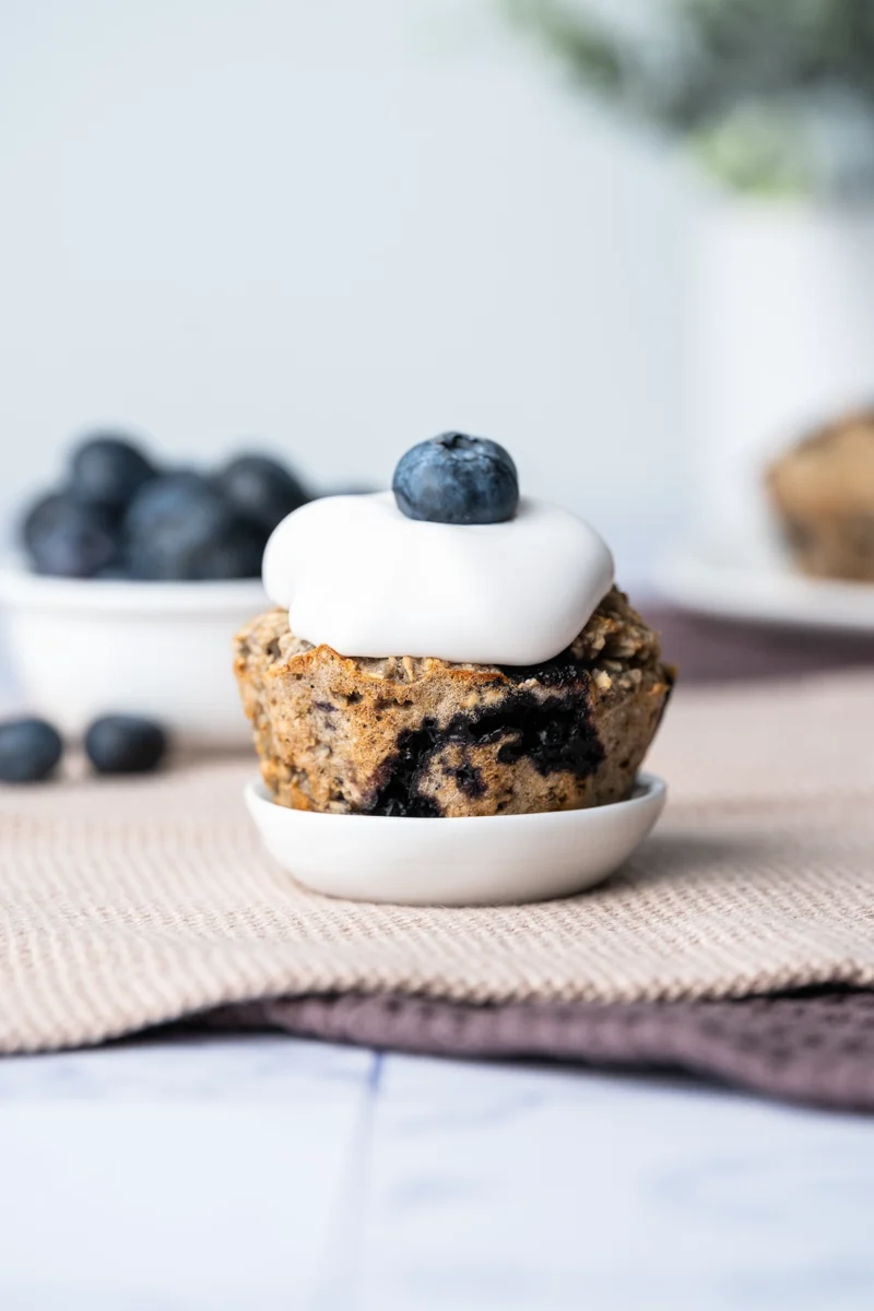 rezept-vegan-muffins-Fruehstueck-gesund-Beeren-3 veganer Blaubeermuffin mit Kokosjoghurt getoppt auf einem ganz kleinen weißen Tellerchen