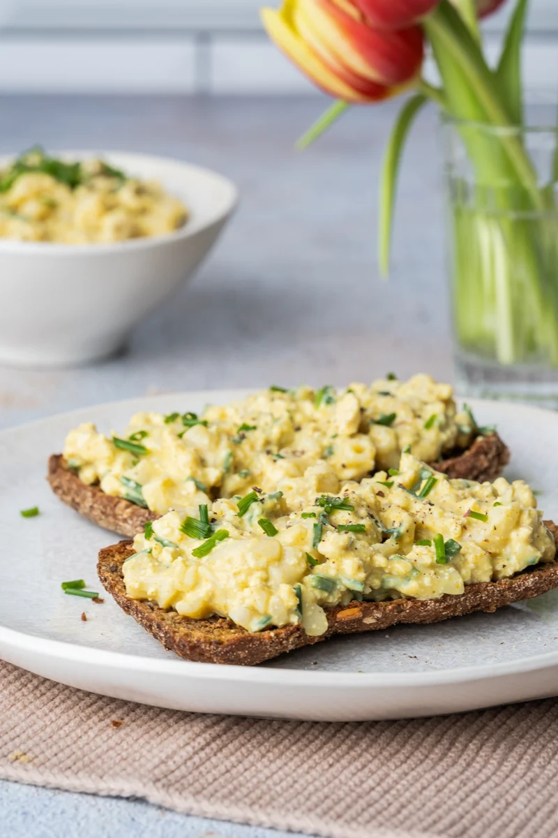 rezept-veganer-eiersalat-oster-kichererbsen Veganer Eiersalat auf 2 dunklen Scheiben Brot auf einem weißen Teller