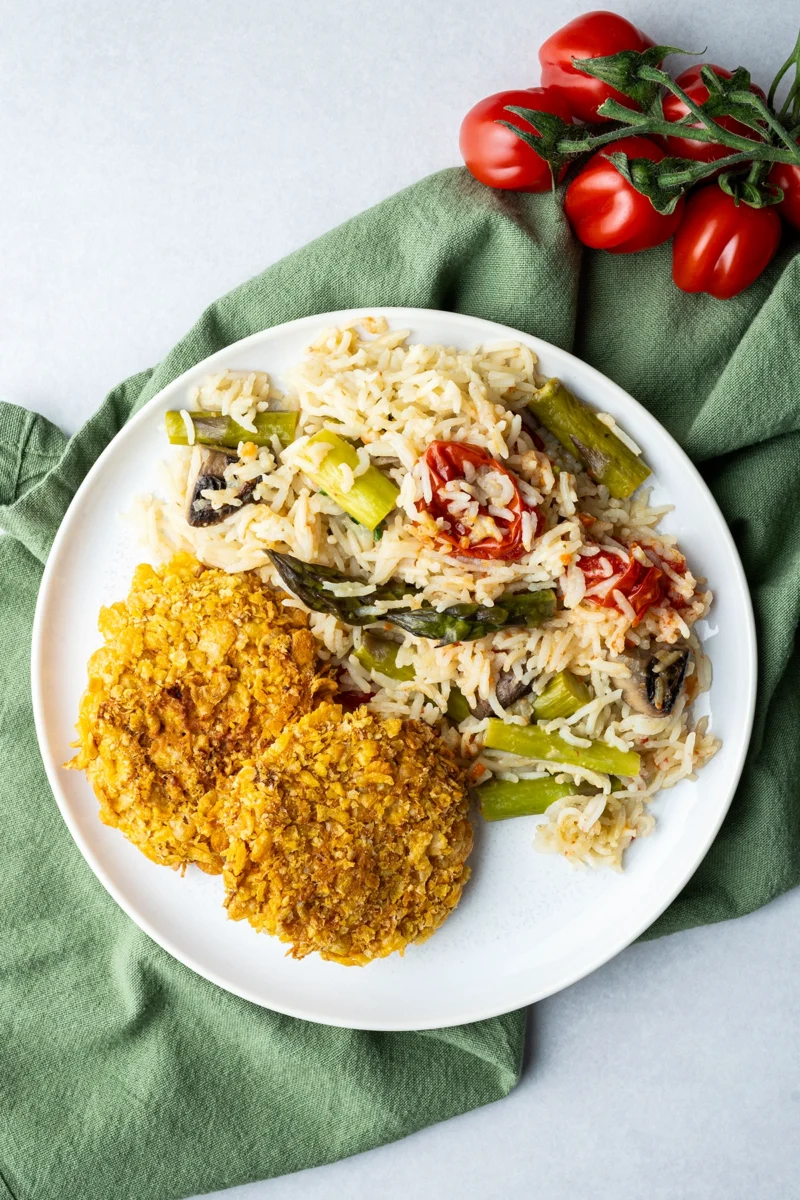 rezept-vegan-ofenreis-spargel-sojaschnitzel Ofenreis mit Gemüse und Sojaschnitzel auf weißem Teller auf grünem Tuch