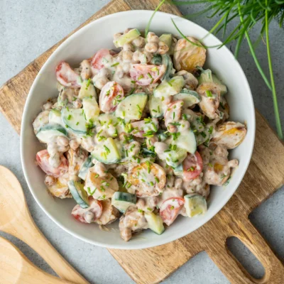 Leichter Kartoffelsalat ohne Mayo in weißer Schale auf Holzbrett