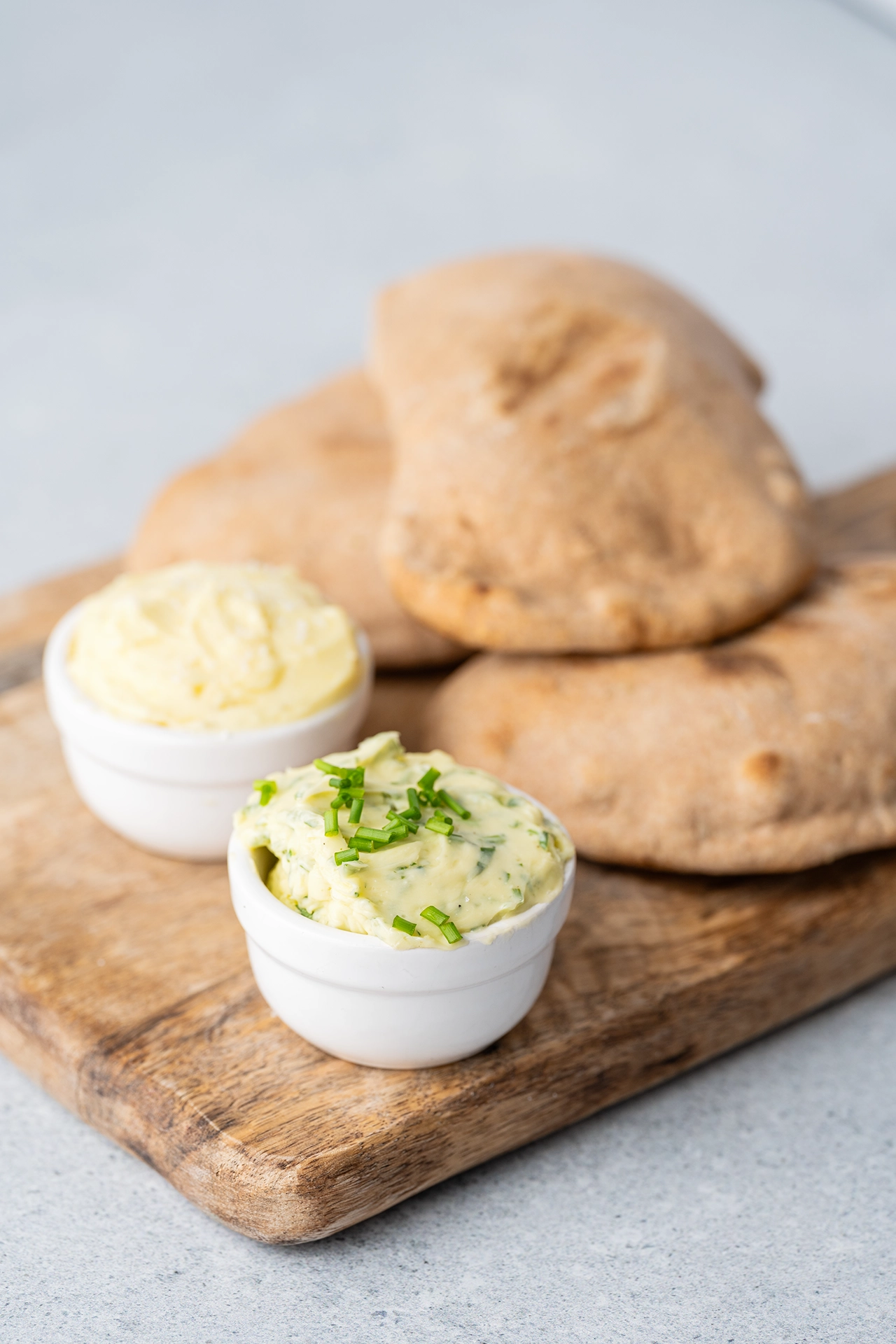 Vegane Kräuterbutter 2 Kräuter- und Knoblaucbutter neben Brot auf Holzbrett