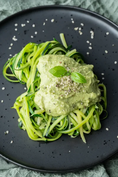 Zucchini-spaghetti mit Avocado-Pesto auf schwarzem Teller