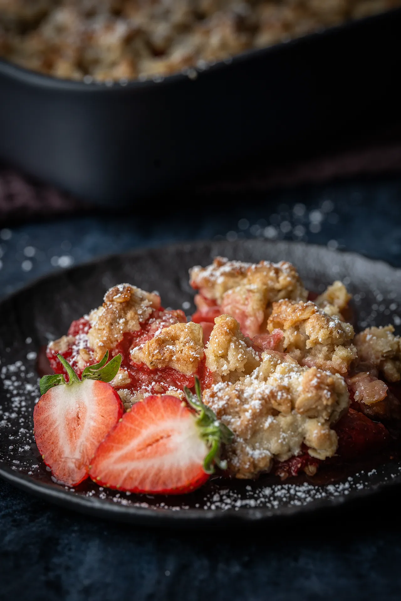 Veganes Erdbeer-Crumble – einfach, süß und unglaublich lecker 1 Veganes Crumble mit Erdbeeren auf einem schwarzen Teller mit Puderzucker