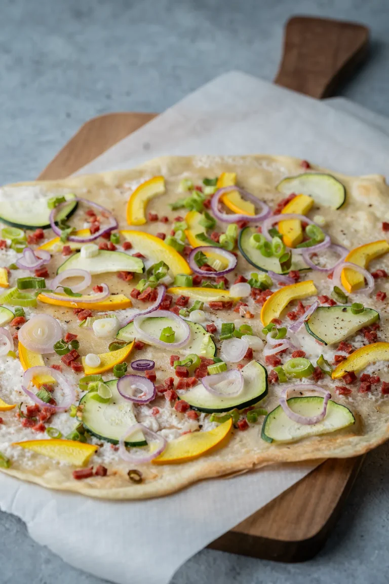Veganer Flammkuchen mit Zucchini und Zwiebeln auf einem Brett