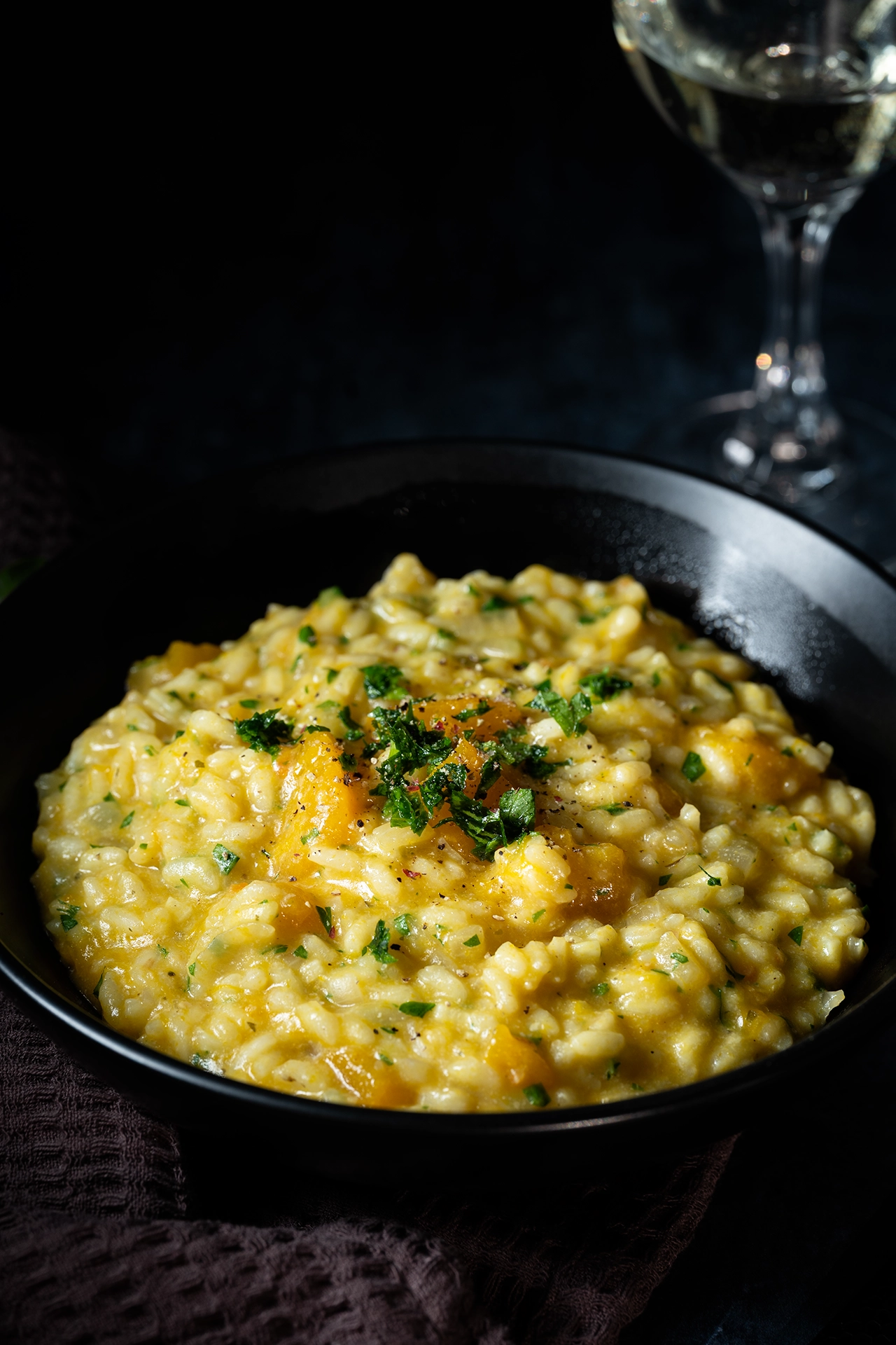 Cremiges Kürbisrisotto 2 Kürbisrisotto auf schwarzem Teller und ein Weinglas