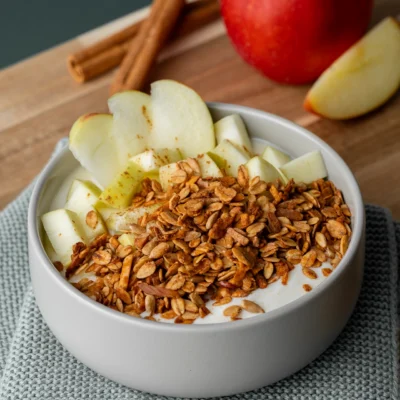 herbstliches Apfel-Zimt-Granola mit Joghurt in einer Schale auf einem Brett