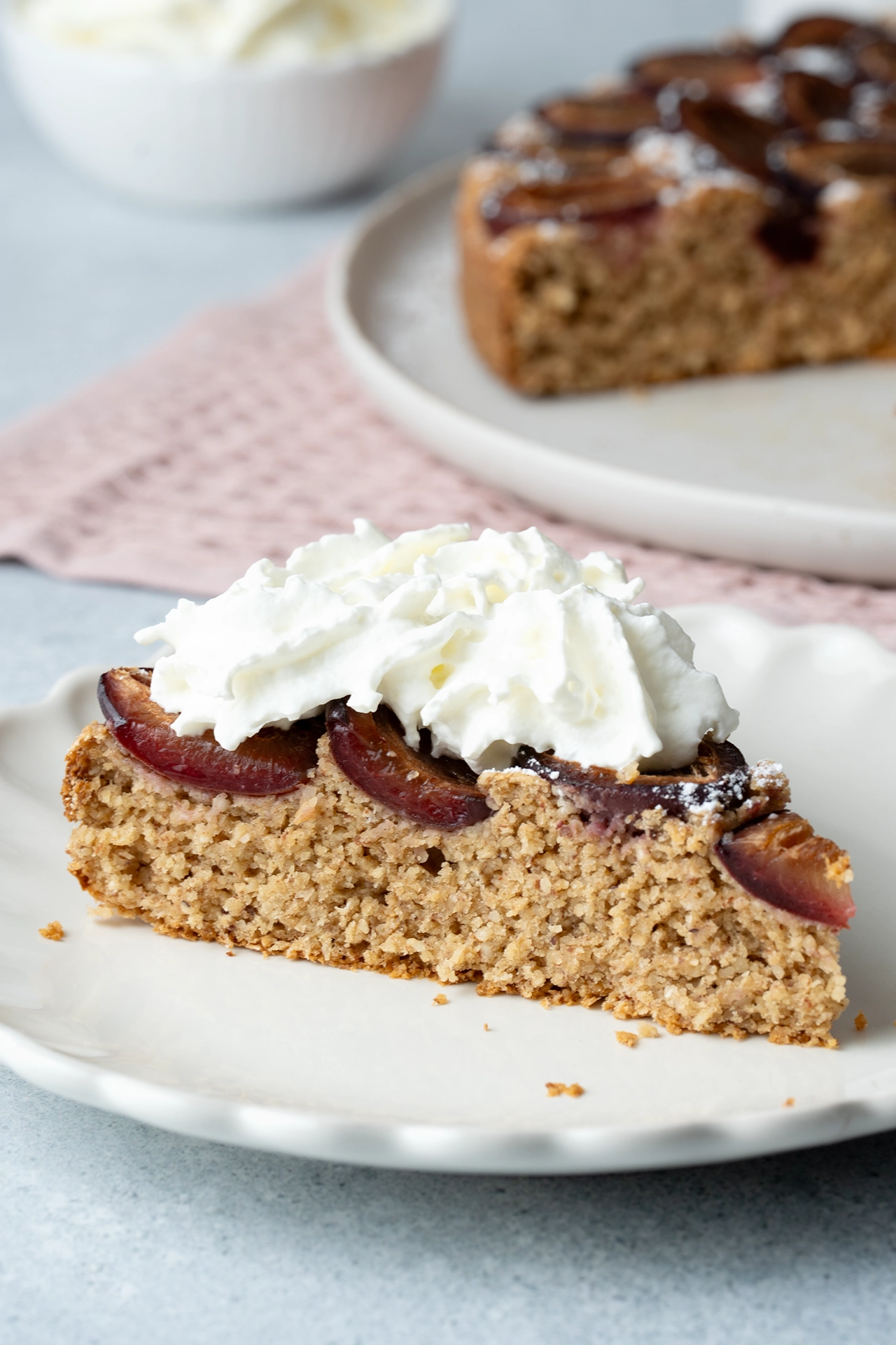 Gesunder Pflaumenkuchen (vegan, glutenfrei und zuckerfrei) 3 ein Stück Pflaumenkuchen mit Sahne auf weißem Teller