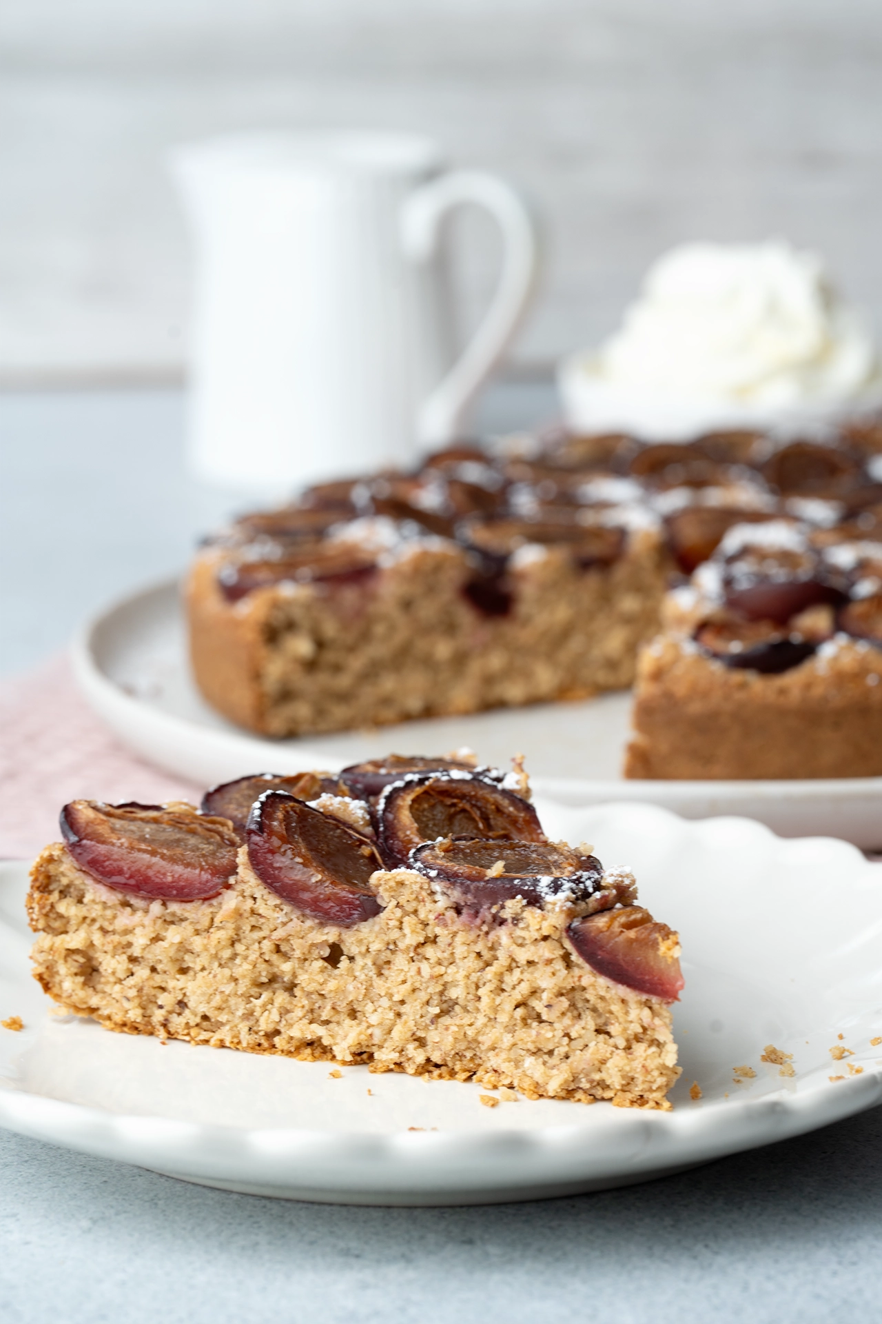Gesunder Pflaumenkuchen (vegan, glutenfrei und zuckerfrei) 4 Zwetschgenkuchen auf einem Teller im Hintergrund der ganze Kuchen