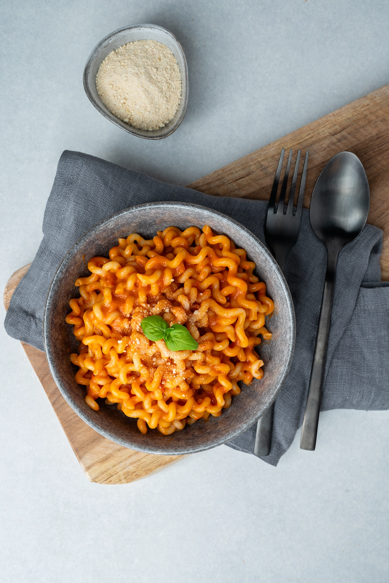 Paprika Pasta in grauer Schale mit dunklem Besteck und Parmesan-Alternative