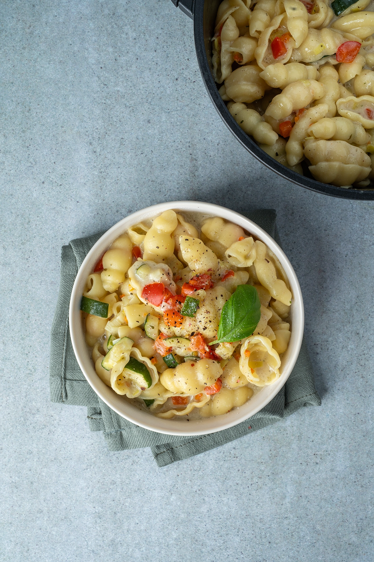 Einfache One Pot Pasta mit Gemüse 2 One Pot Pasta in einer hellen Schale auf einem grün-grauem Tuch