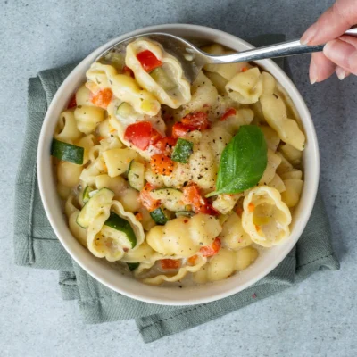 Einfache One Pot Pasta mit Gemüse 4 Einfache One-Pot-Pasta in einer hellen Schale, eine Hand hält einen Löffel