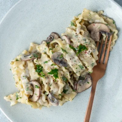 Vegane Champignon-Nudeln auf hellem Teller mit Gabel