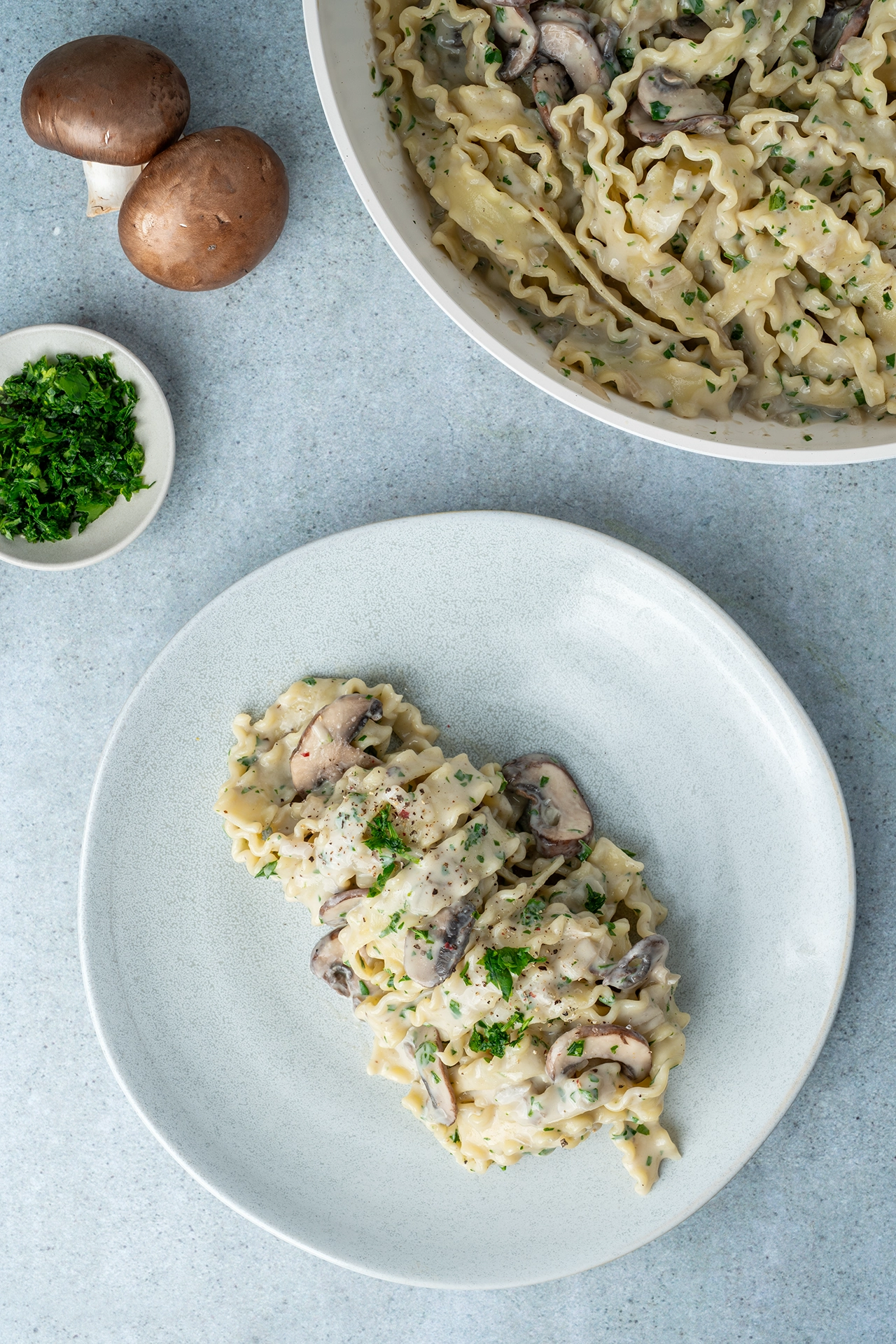 Nudeln mit veganer Champignonsoße auf einem Teller, daneben Petersilie und 2 Pilze