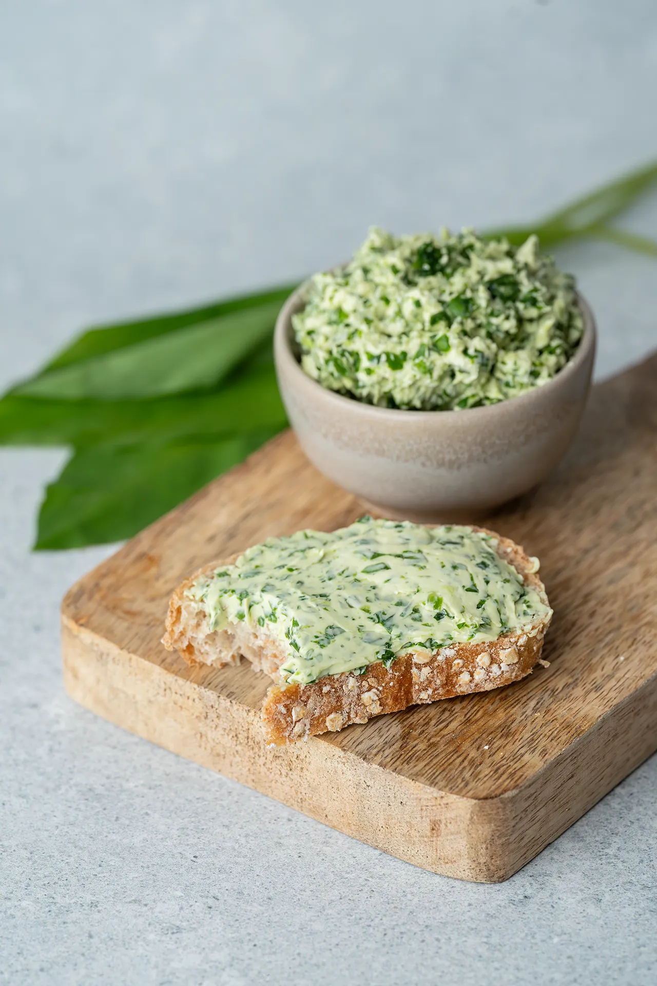Bärlauchbutter in einem Töpfchen und auf einem Brot auf einem Brett
