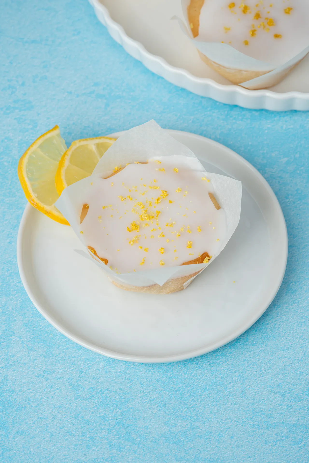 Zitronenmuffin in weißem Papier mit Zuckerguss auf weißem Teller