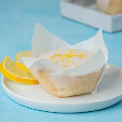 Zitronen-Muffin auf weißem Teller daneben Zitronenscheiben