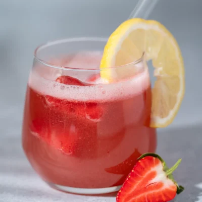 Erdbeer-Zitronen-Limo – gesunde Sommerlimonade zum Einfrieren 5 Erdbeer-Zitronen-Limonade in einem Glas mit einer Zitronen Scheibe und daneben eine Erdbeere