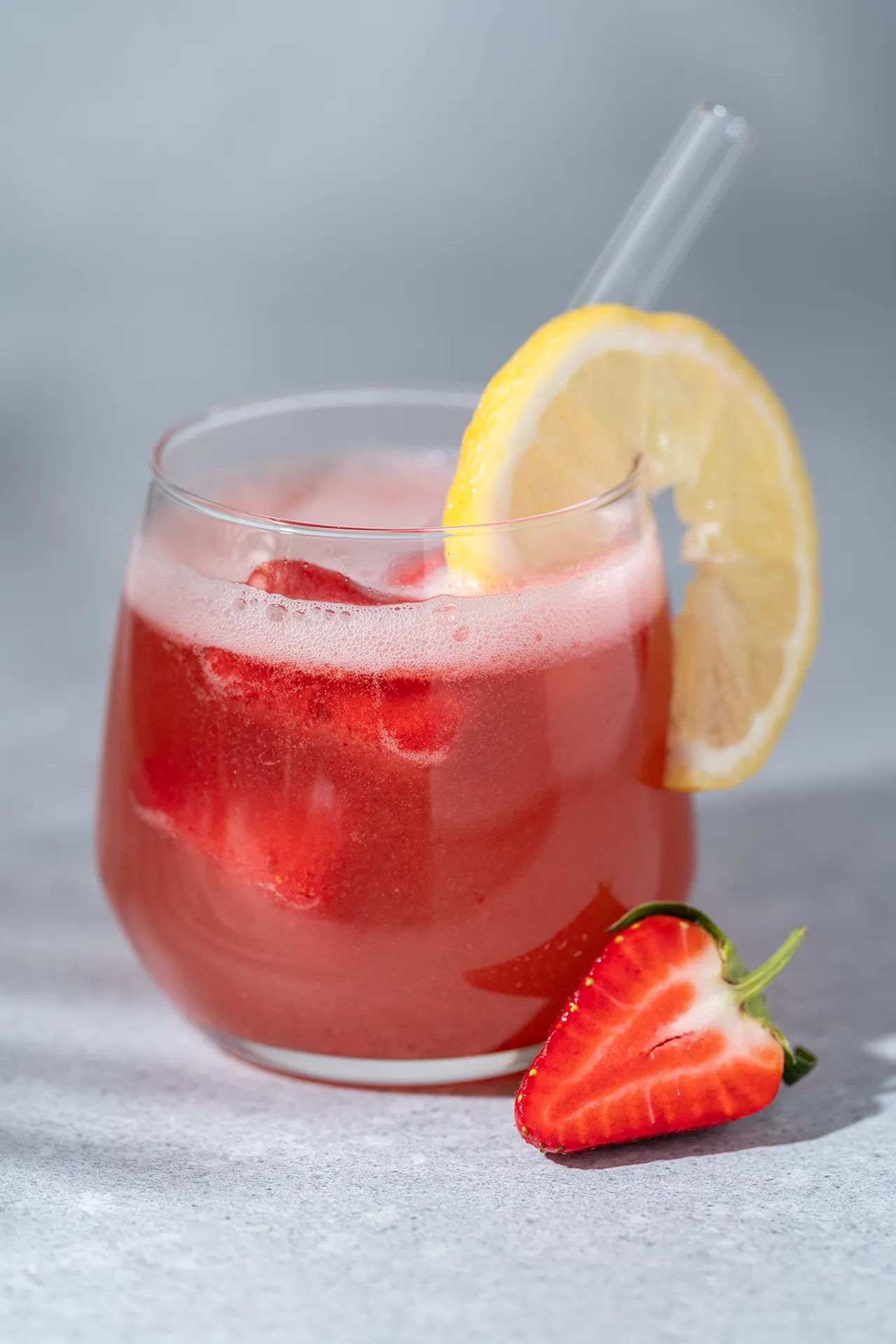 Erdbeer-Zitronen-Limo – gesunde Sommerlimonade zum Einfrieren 1 Erdbeer-Zitronen-Limonade in einem Glas mit einer Zitronen Scheibe und daneben eine Erdbeere