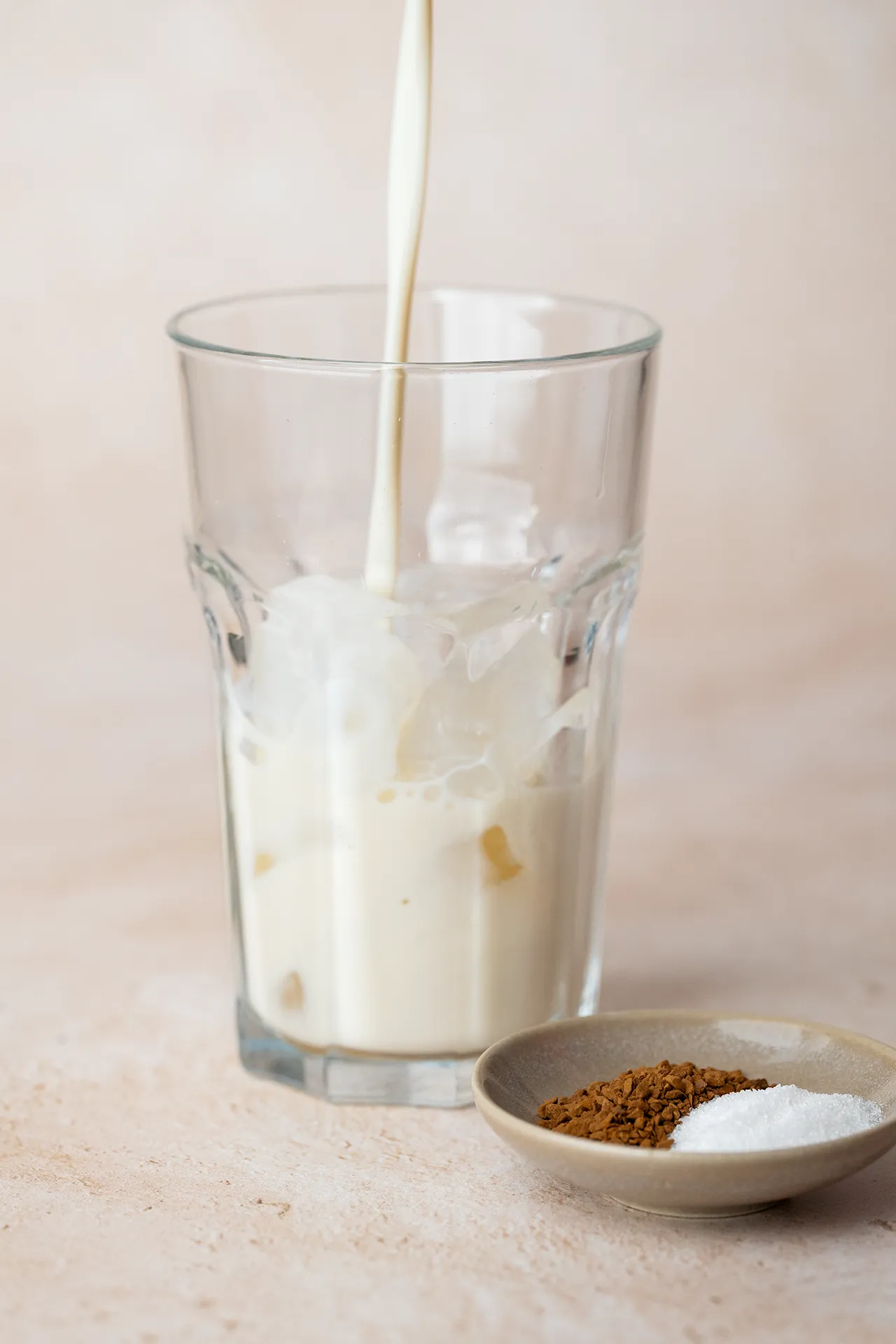 Eiskaffee mit Instantkaffee – einfaches Rezept in 2 Minuten 1 Ein Glas mit Eiswürfeln und Milch, daneben Instantkaffee und Zucker