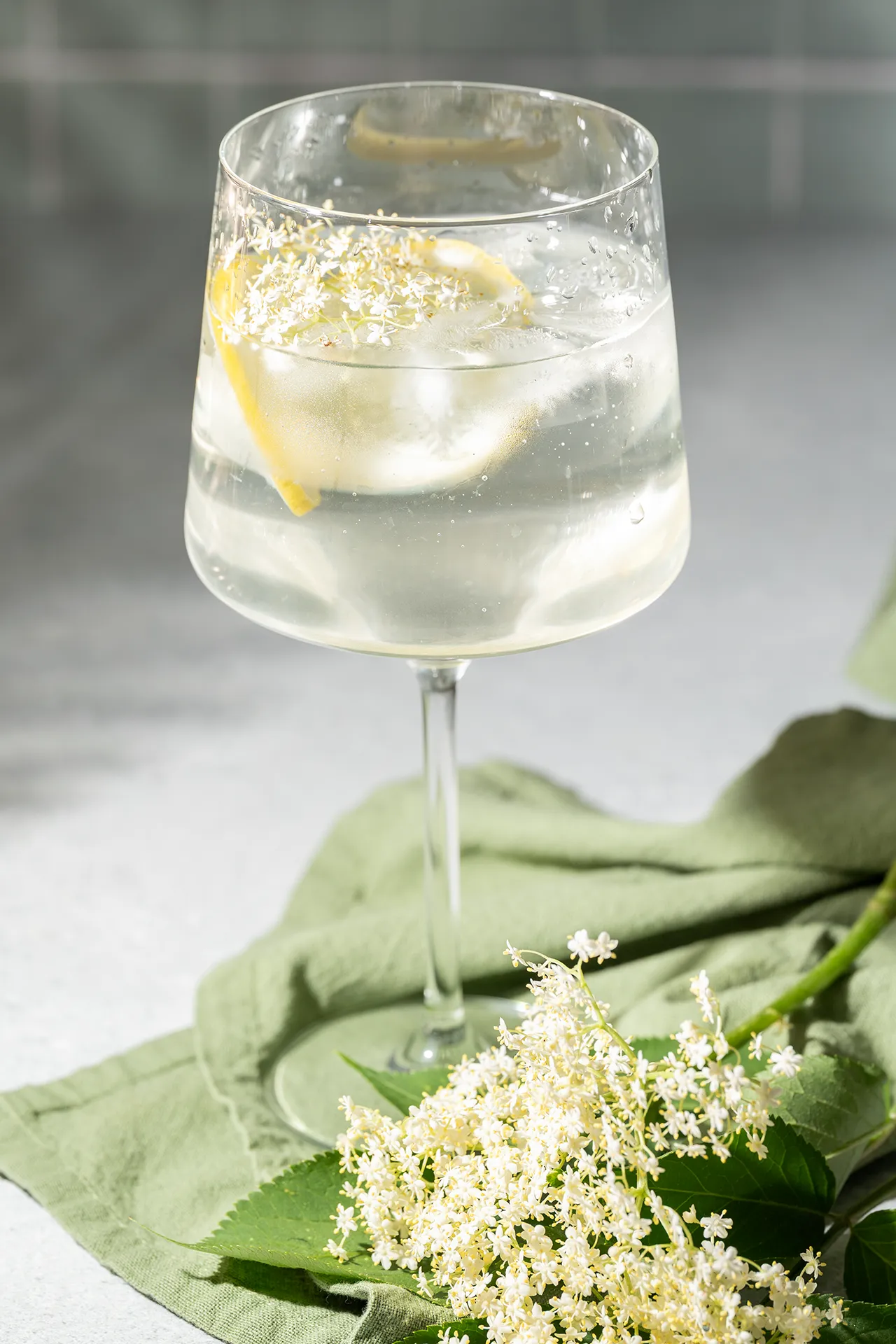 Holunderblütensirup selber machen – einfaches Rezept für den Sommer 3 Holunderblütensirup mit Zitrone und Wasser in einem Glas, daneben eine Holunderblütendolde