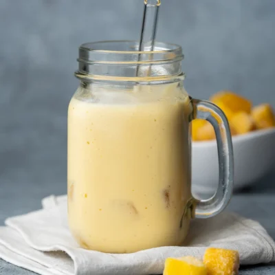 Veganer Mango Lassi in einem Glas mit Trinkhalm, daneben Mangostücke