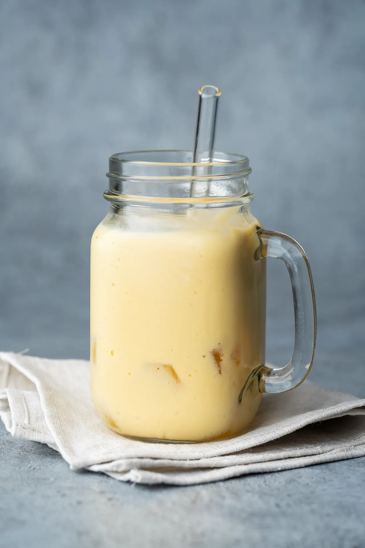 Veganer Mango Lassi – einfaches Rezept mit nur 4 Zutaten 1 Mango Lassi vegan in einem Glas auf mit Henkel und Trinkhalm