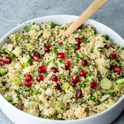 Startseite 13 Couscous-Salat mit Kräutern, Zitrone und Granatapfelkernen in einer weißen Schale mit Holzlöffel