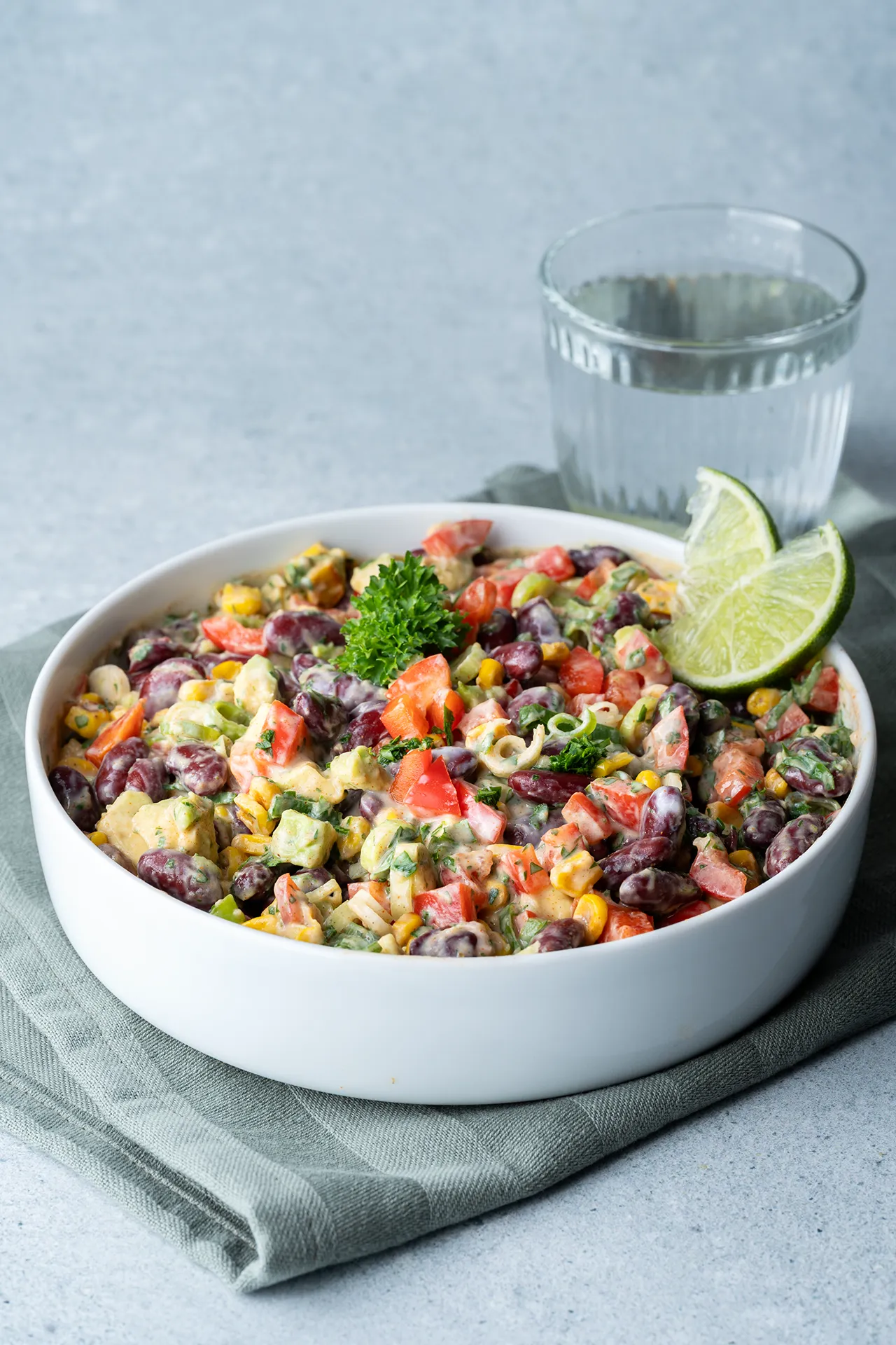 Mexikanischer Maissalat mit Bohnen und Avocado - einfach und sättigend 1 Mexikanischer Maissalat mit Limette in einer weißen Schale daneben ein Wasserglas