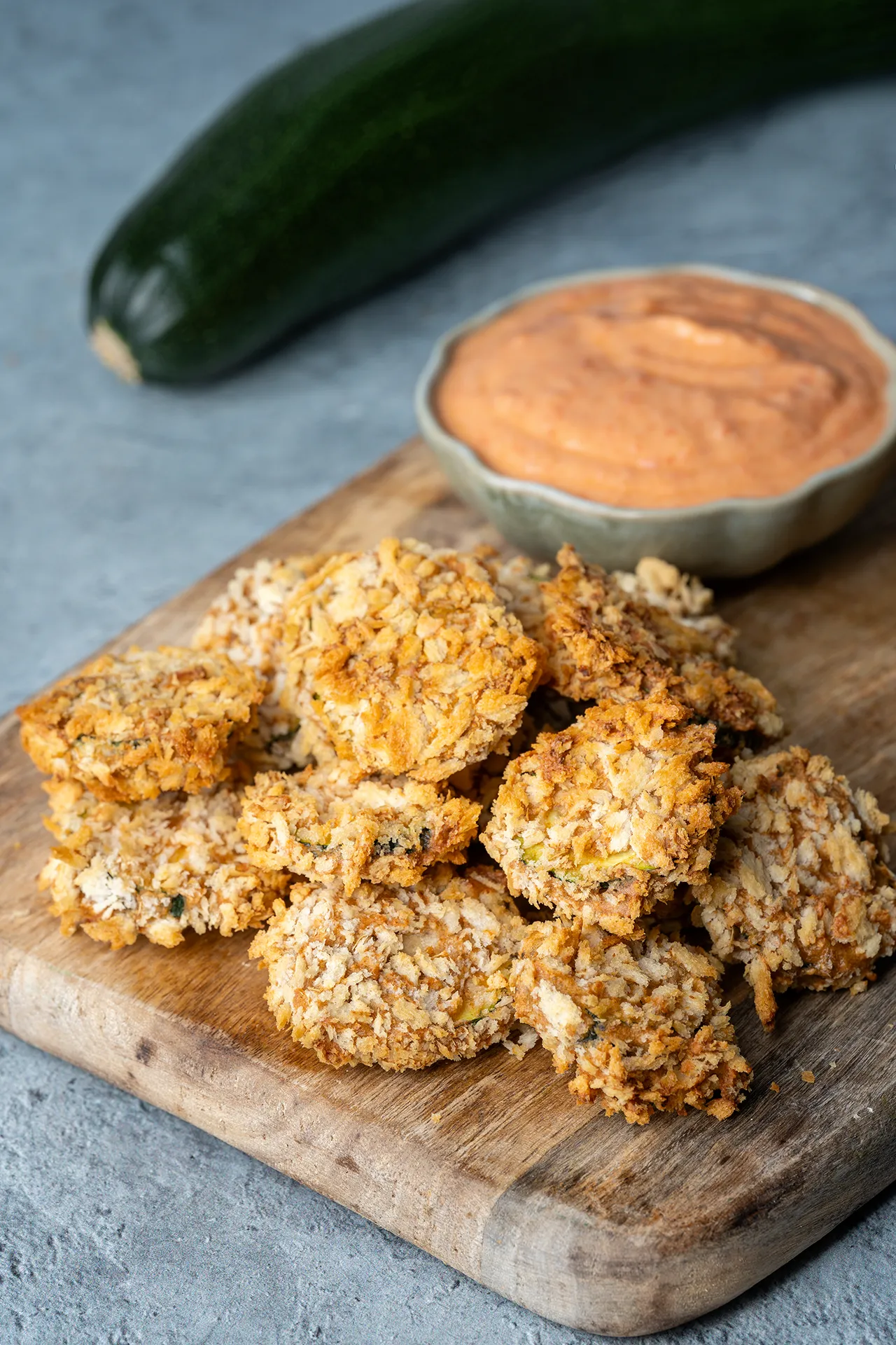 Knusprige Zucchini-Scheiben aus dem Airfryer auf einem Brett mit Dip