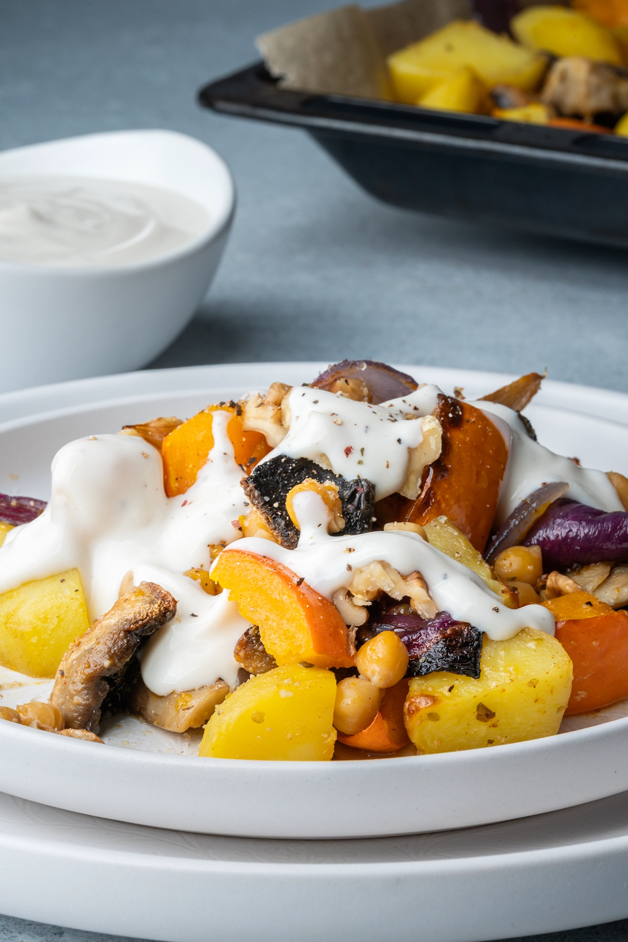 Kürbis-Kartoffel-Blech mit Kichererbsen und Knoblauchjoghurt 3 Kürbis-Kartoffel-Blech mit Kichererbsen und Knoblauchjoghurt auf einem weißen Teller neben dem Blech
