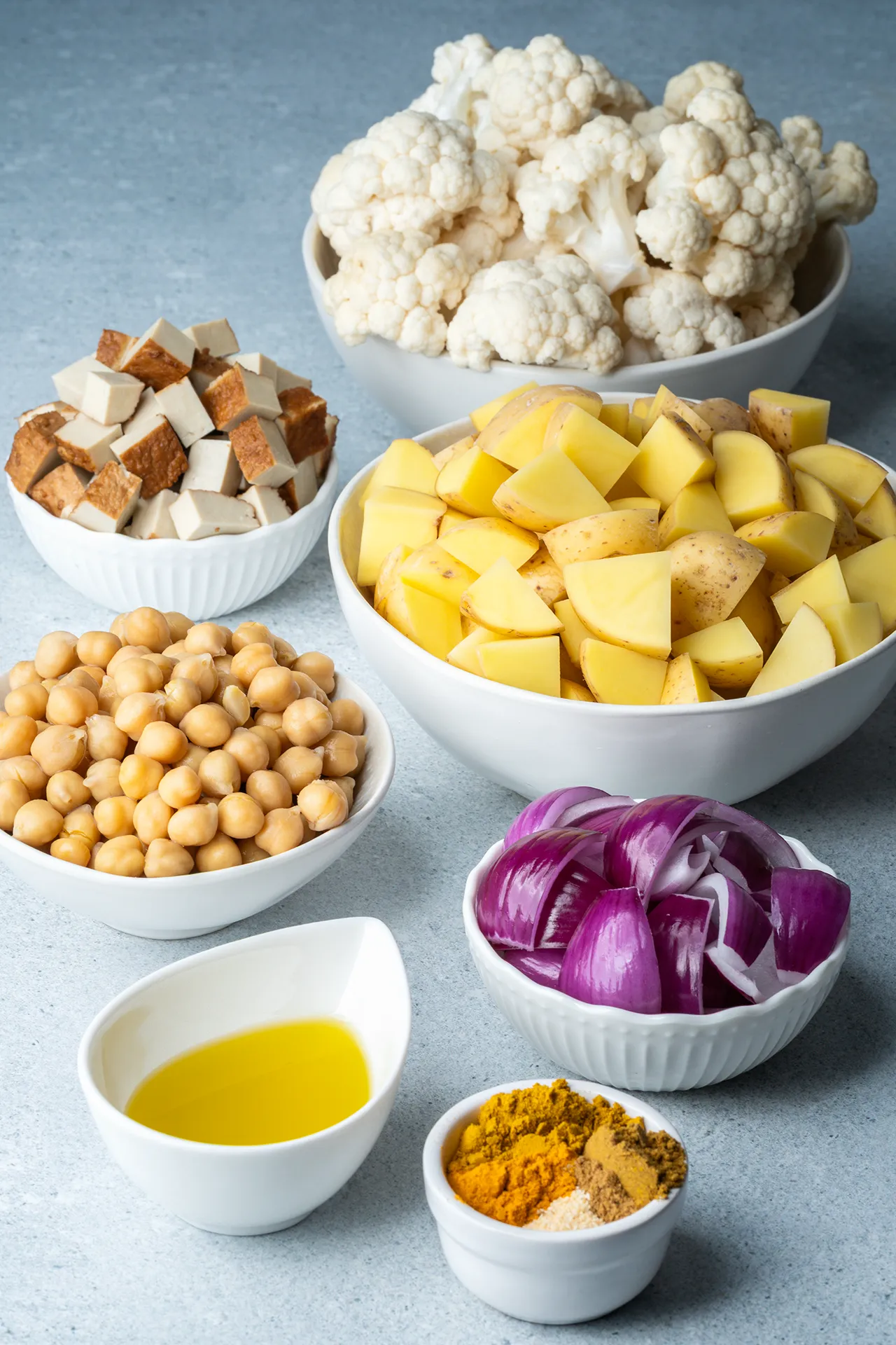 Curry-Blech mit Blumenkohl und Kichererbsen 2 Kartoffeln, Blumenkohl, Kichererbsen, Zwiebeln, Tofu und Gewürze in einzelnen weißen Schalen