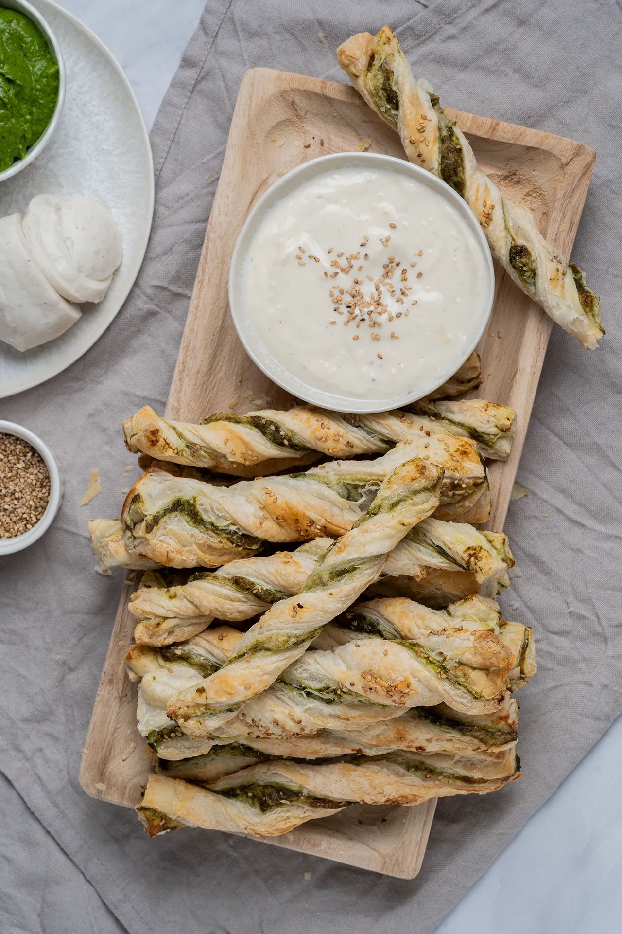 gedrehte Blätterteigsticks mit Spinatcreme auf einem Holzbrett mit einer Schale weißem Dip
