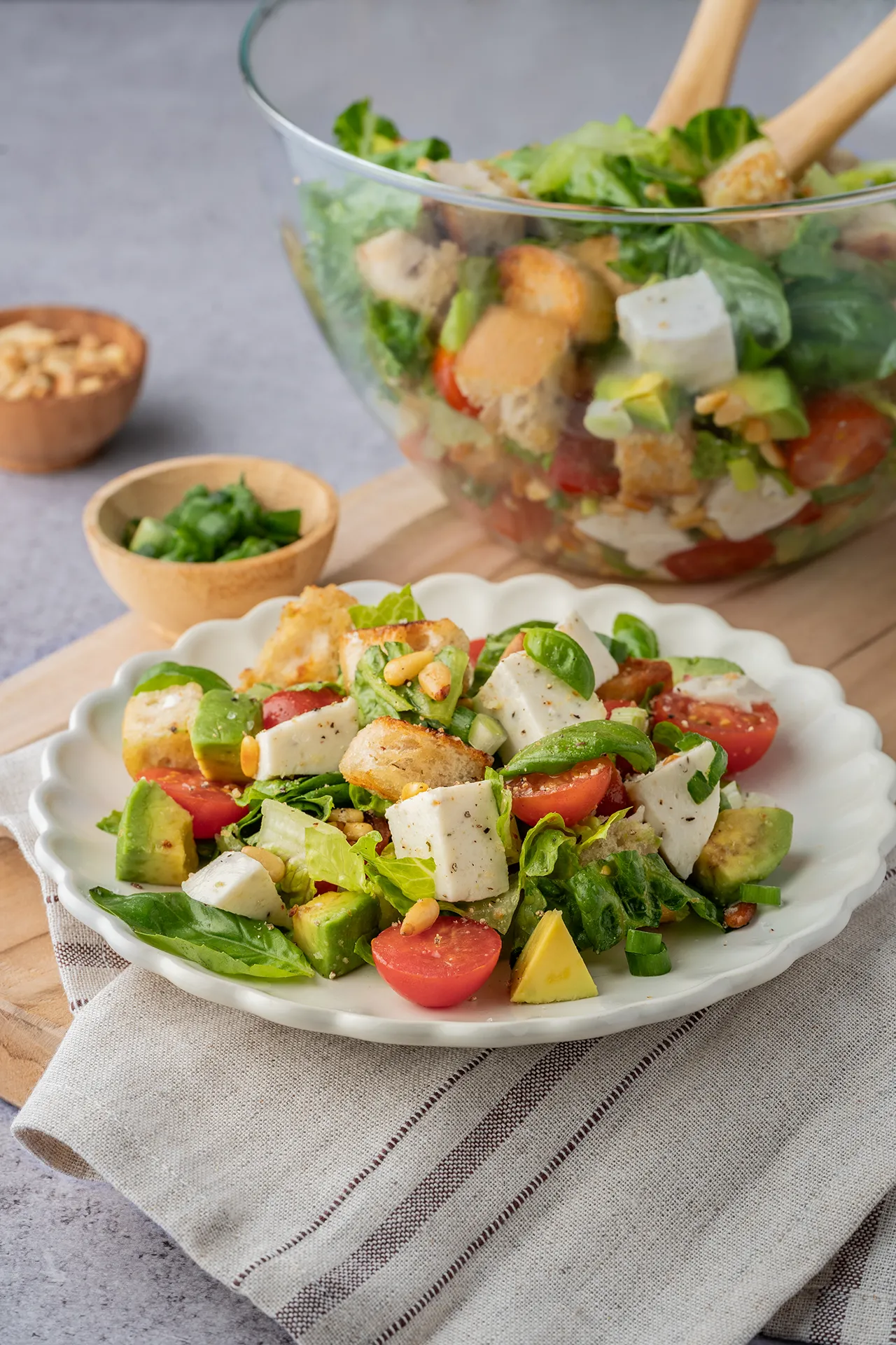 Brotsalat mit Mozzarella auf einem weißen Teller dahinter in einer Glasschale
