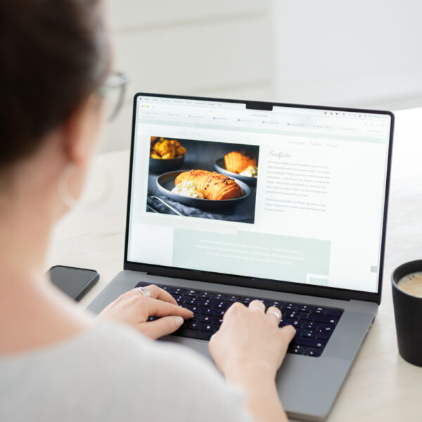 Laptop daneben eine schwarze Tasse mit Kaffee