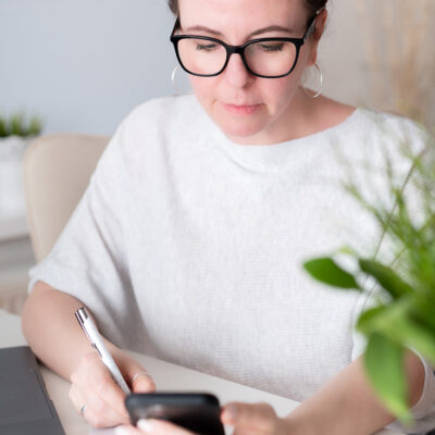 Katja am Schreibtisch mit Handy in der Hand und einem Kugelschreiber