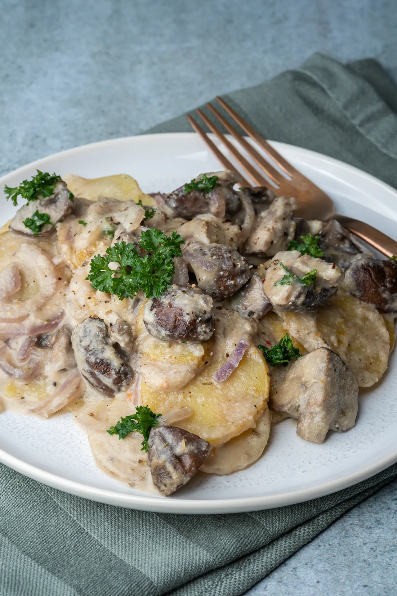 Kartoffel-Champignon-Auflauf in cremiger Knoblauchsoße 2 Kartoffel-Champignon-Auflauf ohne Sahne mit einer Gabel auf einem Teller
