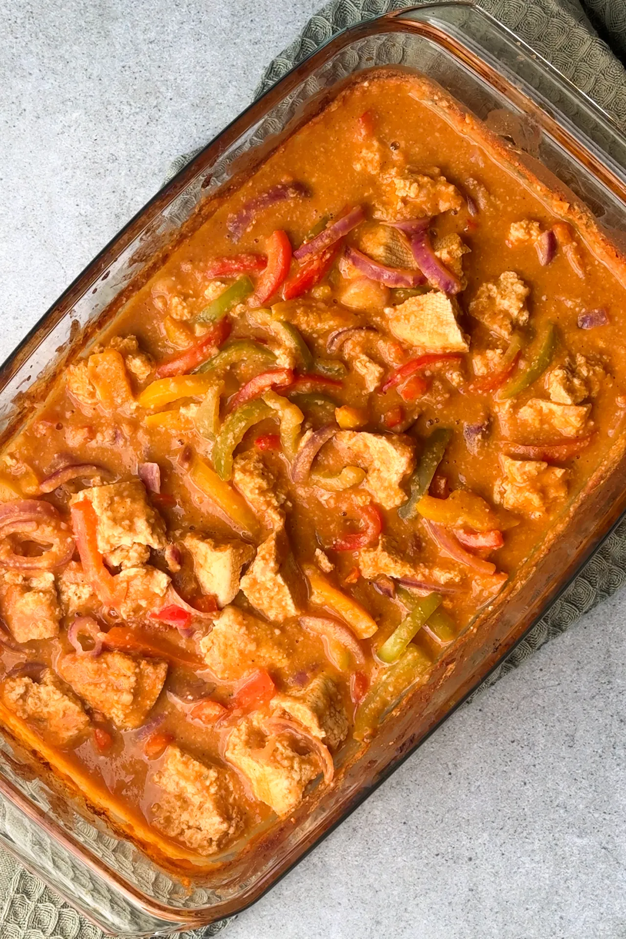 Veganes Paprika-Sahne-Hähnchen mit Tofu – ganz ohne Sahne 2 Eine Auflaufform aus Glas mit Paprika-Sahne-Hähnchen mit Tofu auf grünem Tuch